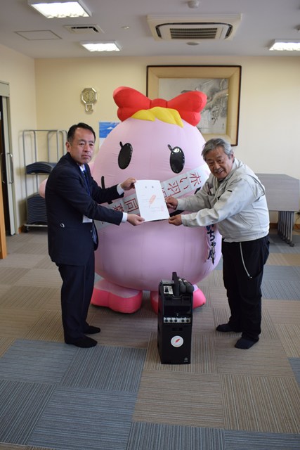 あいちゃんを背景に、岡谷市共同募金委員会事務局長から上浜区区長へ目録が渡される様子