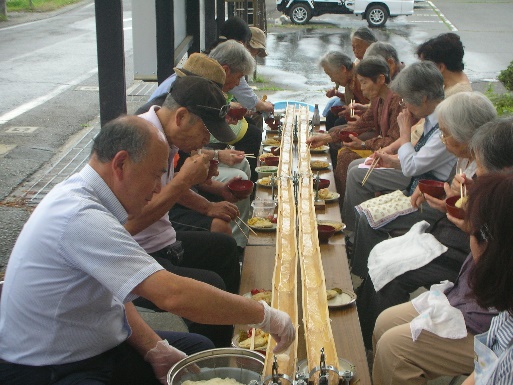 両側にそうめんをすする高齢者、そうめんを流す区長とともに