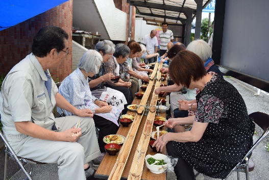 流しそうめんを楽しむ様子、両側には人が並ぶ